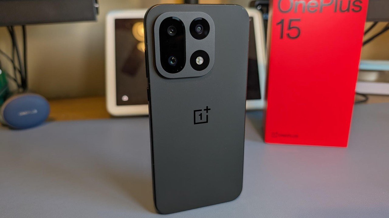 책상 위에 세워 둔 OnePlus 15 스마트폰과 붉은 제품 상자